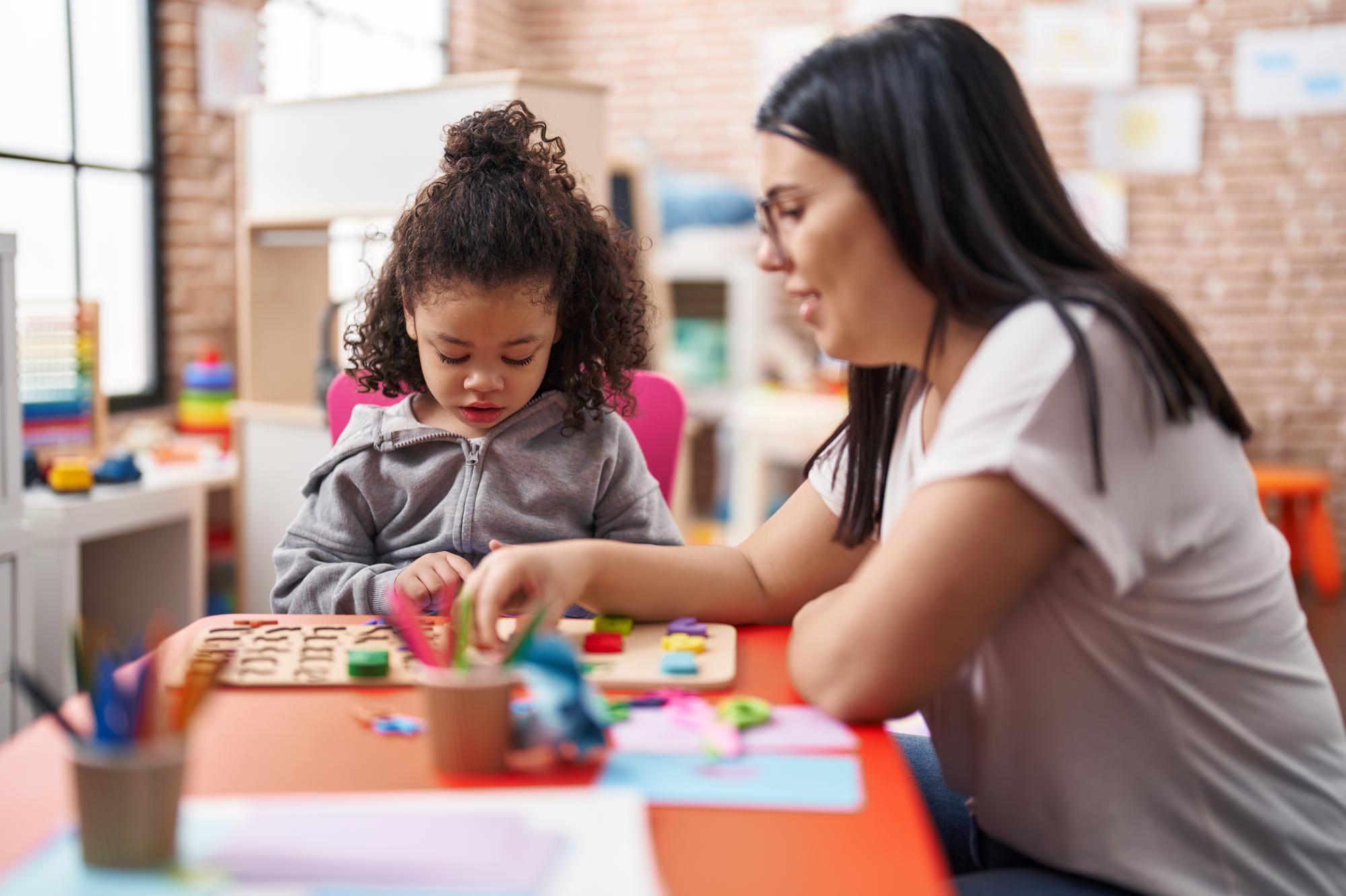 Maestra y niño pequeño jugando con un juego de rompecabezas